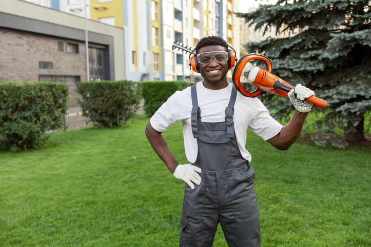 Professional black tree trimmer smiling with equipment in commercial landscaping setting